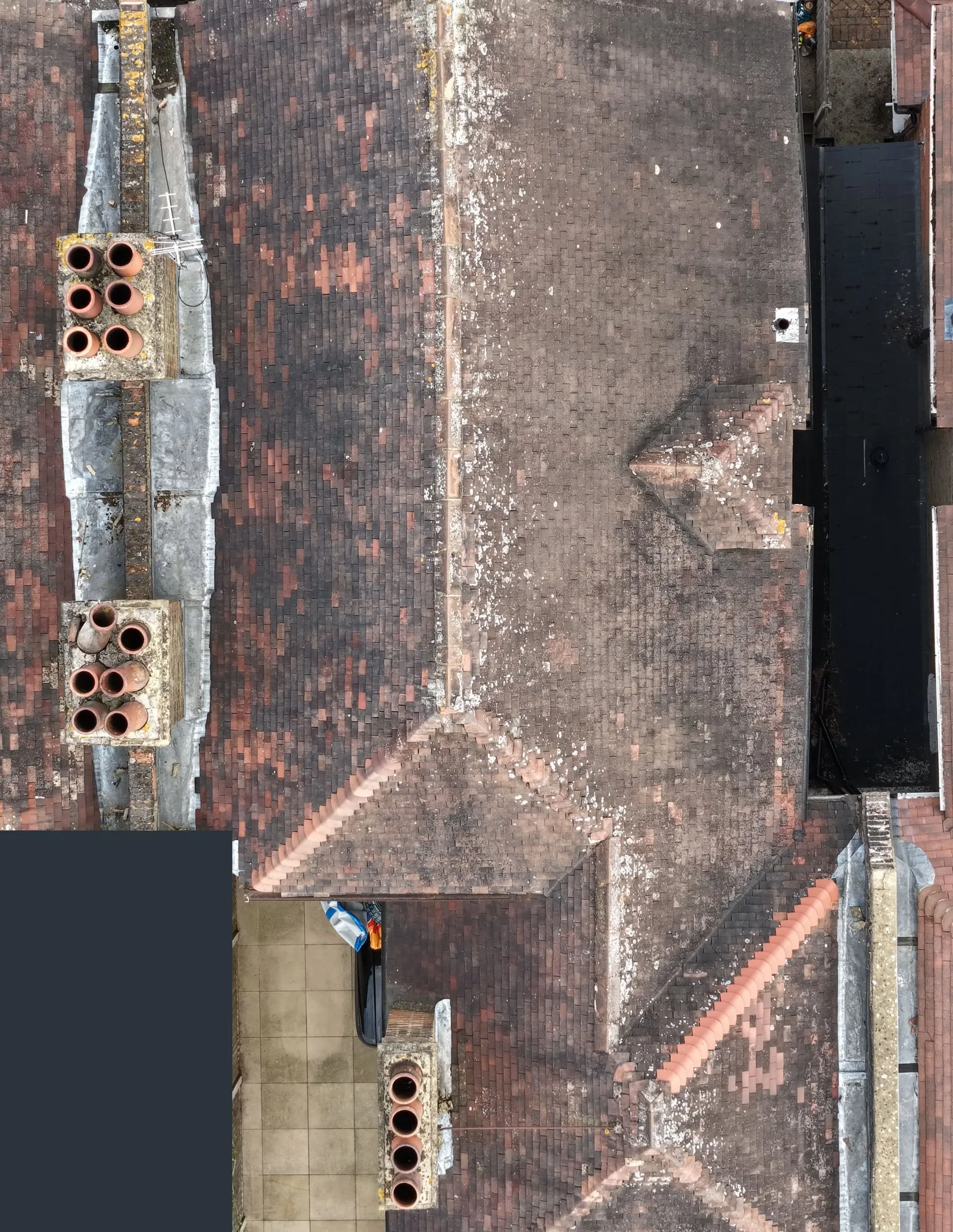 Top-down drone photo of a tiled terraced-house roof, with two chimney stacks on its left-hand party wall and a side return roof on its right