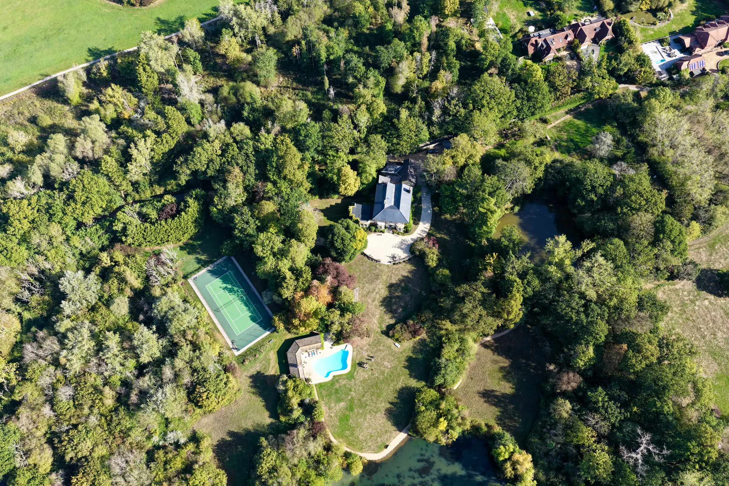 Aerial view of the estate's grounds, including a tennis court, swimming pool and pond surrounded by mature trees