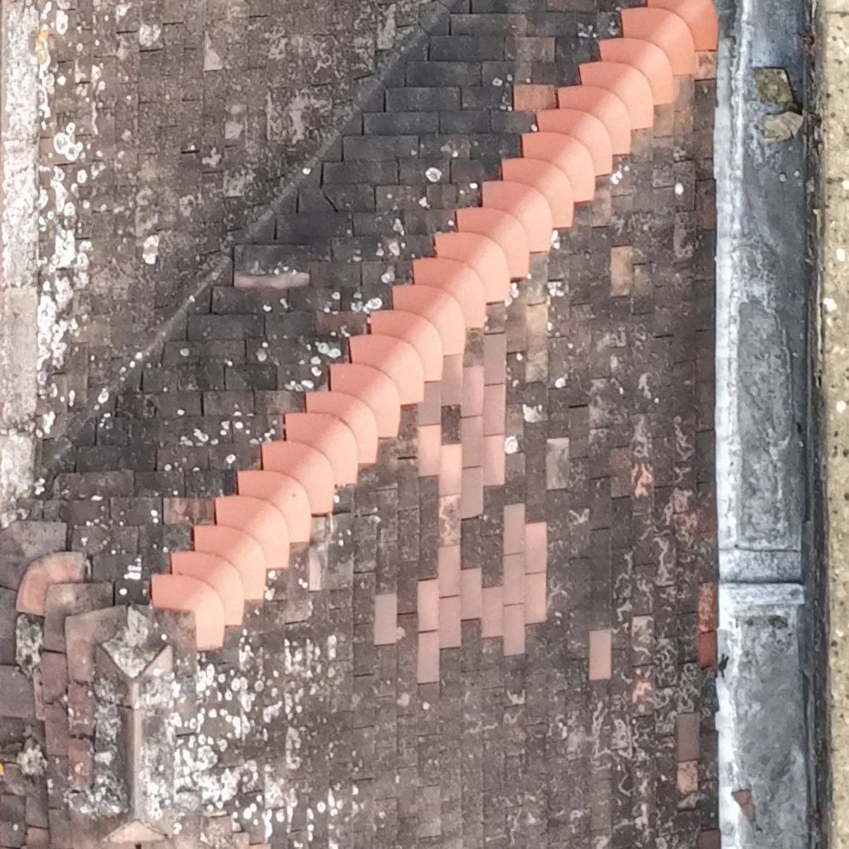 Close-up of a roof hip with a line of bright orange hip tiles and a patch of lighter replacement tiles beside it