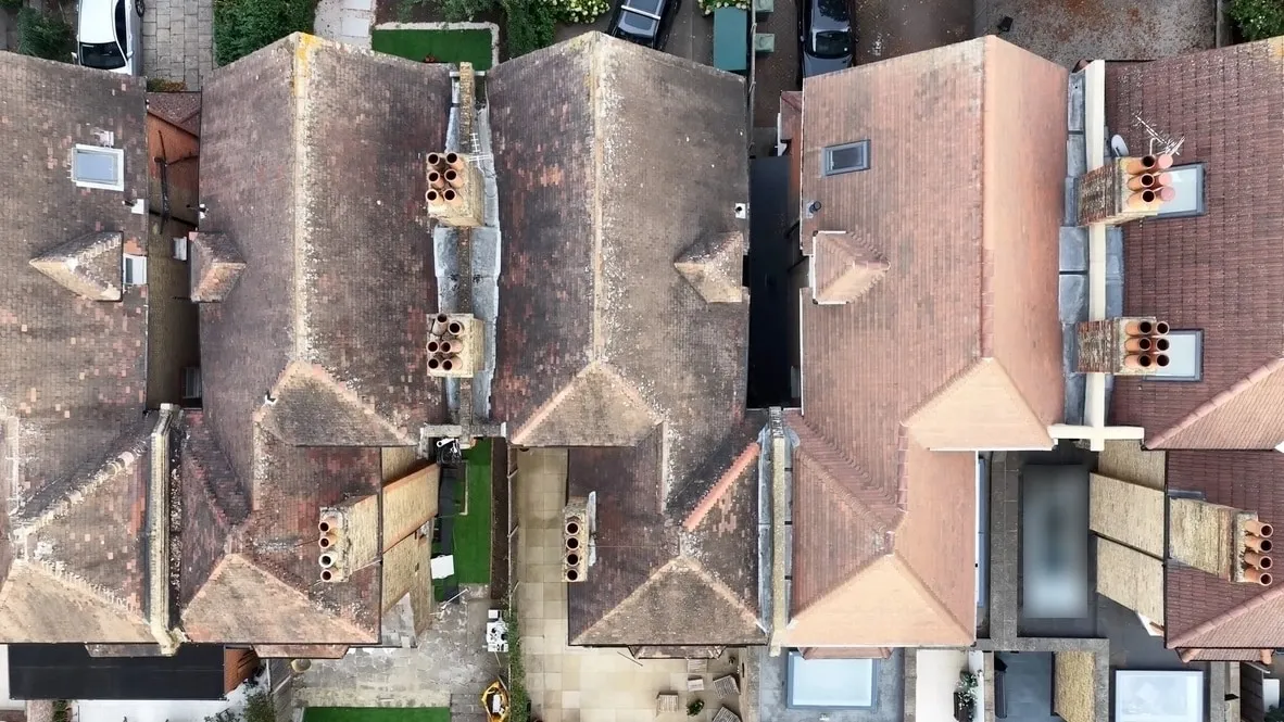 Top-down drone photo of a row of London house roofs, showing tiled roof slopes, chimney stacks, a dormer and roof windows
