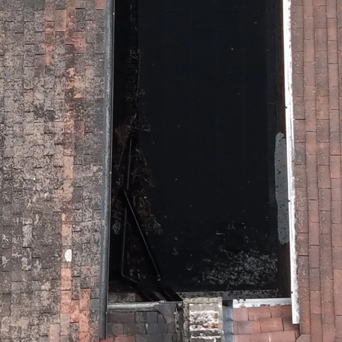 Close-up of a dark side return roof beside a tiled slope, with leaves and debris collected at one end