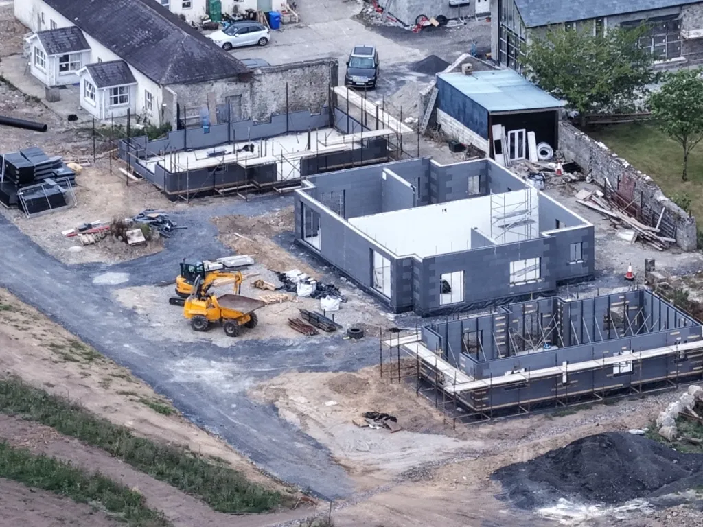 Close aerial view of a new building's concrete and steel frame under construction, with a digger and building materials on site