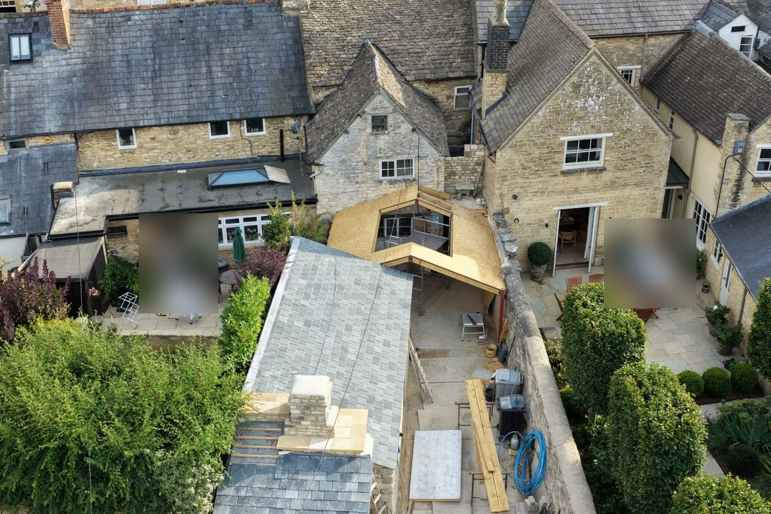 Aerial view of the same extension mid-build, with the timber frame and roof structure visible and two people blurred for privacy