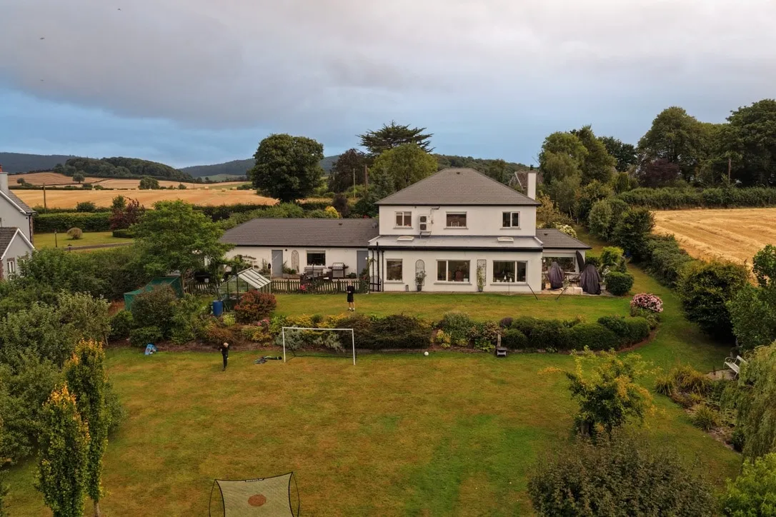 Aerial view of a white rendered house and garden in the countryside, with fields visible beyond