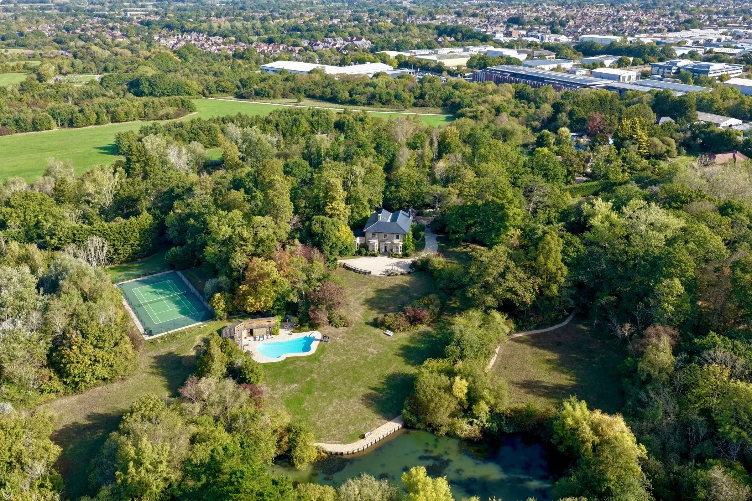 Aerial view of the whole estate, with the house among trees and the tennis court, swimming pool and pond in its grounds